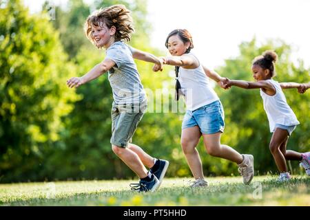 Les enfants se tenant la main et courir dans le parc, en souriant. Banque D'Images