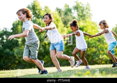 Les enfants se tenant la main et courir dans le parc, en souriant. Banque D'Images