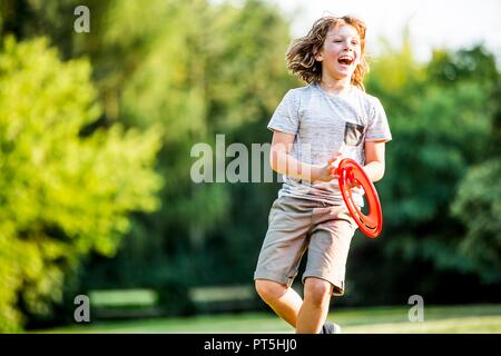 Garçon jouant avec disque volant en parc, à rire. Banque D'Images