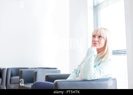 Pensive Mid adult woman sitting in salle d'attente du médecin avec la main sur le menton. Banque D'Images