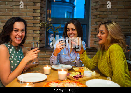 Trois femmes friends toasting with red wine dans la cuisine. L'accent sur la femme moyenne Banque D'Images