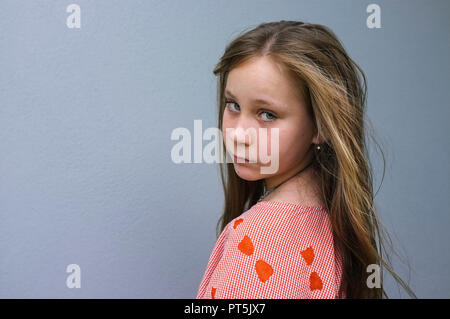Portrait d'une fille préadolescente à par-dessus son épaule, contre un mur gris. Banque D'Images