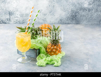 Cocktail à l'ananas dans deux verres en verre avec de la glace et deux mini ananas sur fond gris Banque D'Images