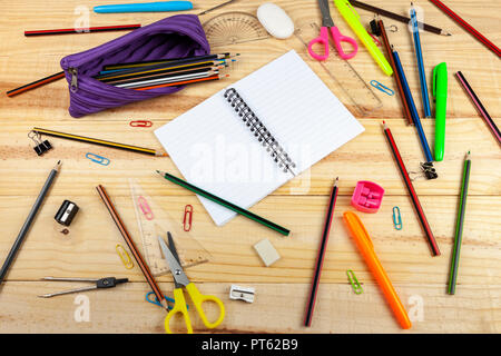 Note des pages de livre blanc bordée sur une école en bois bureau avec un crayon violet cas et dispersés des crayons et ciseaux Banque D'Images