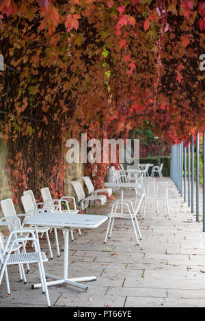 Romantique vieille ruelle en pierre avec la chute de lierre et rouge blanc, métal, chaises et tables vides dans un style vintage Banque D'Images