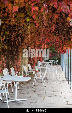 Romantique vieille ruelle en pierre avec la chute de lierre et rouge blanc, métal, chaises et tables vides dans un style vintage Banque D'Images