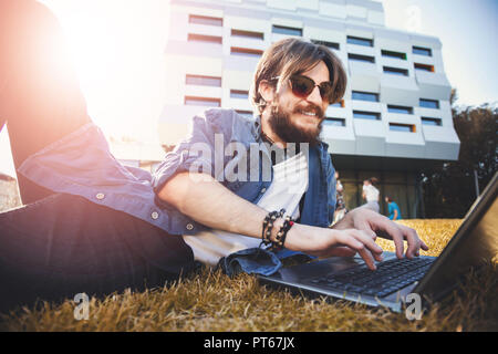 Bel homme étudiant barbu portant des lunettes situées près de l'université et d'étudier avec l'ordinateur portable, l'étude de conception Banque D'Images