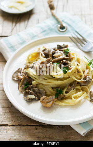 Tagliatelles à la crème et champignons des bois sauce dans une assiette blanche sur un fond de bois. Style rustique. Banque D'Images