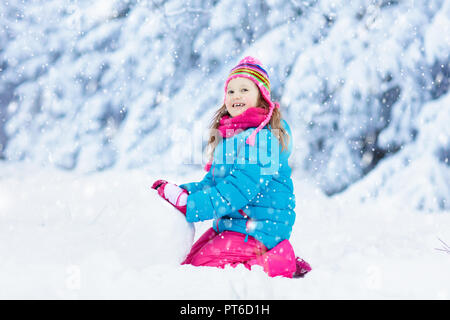 Kid faire bonhomme de neige dans le parc d'hiver. Les enfants jouent dans la neige. Petite fille en veste colorée et hat building bonhomme de neige dans le jardin d'hiver après l'snowfa Banque D'Images