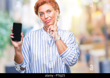 Atrractive young redhead femme montrant l'écran du smartphone sur fond isolé visage sérieux de penser à question, idée très confus Banque D'Images