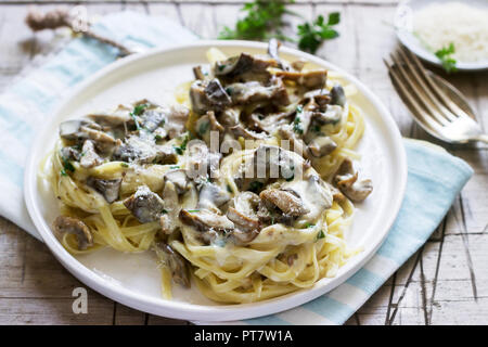 Tagliatelles à la crème et champignons des bois sauce dans une assiette blanche sur un fond de bois. Style rustique. Banque D'Images