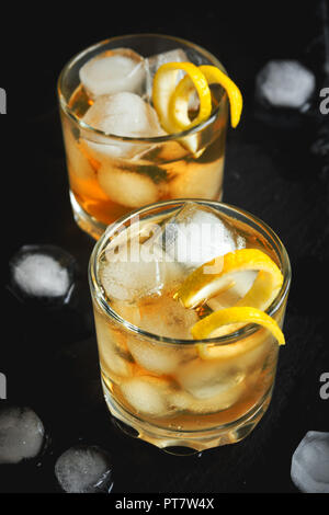 Whiskey ou de rhum sur les roches avec de citron sur fond noir en noir. Banque D'Images