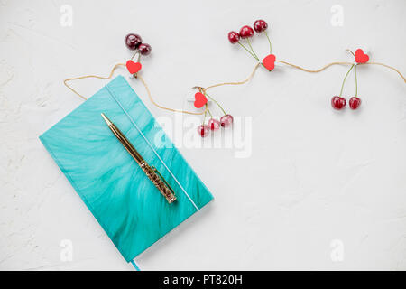Bloc-notes avec stylo et baies sur un tableau blanc avec de l'espace pour le texte.Le petit-déjeuner pour une petite amie.composition décorative de fleurs de saison, de cerise, d'art et matériaux de bureau, le coeur.thème rêve Banque D'Images