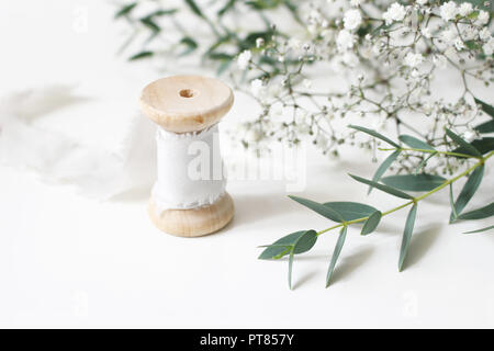 Scène floral féminin. Close-up du tiroir de ruban de soie, de l'Eucalyptus parvifolia feuilles et fleurs Gypsophyla babys souffle sur un arrière-plan du tableau blanc. La décoration de mariage photographie de stock. Selective focus Banque D'Images