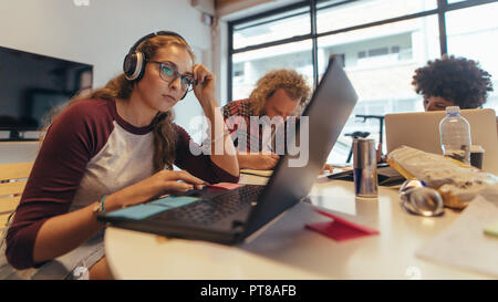 Femme tech professional working on laptop avec des collègues travaillant à l'arrière. Les ingénieurs logiciels travaillant à l'espace de coworking à tech démarrage. Banque D'Images