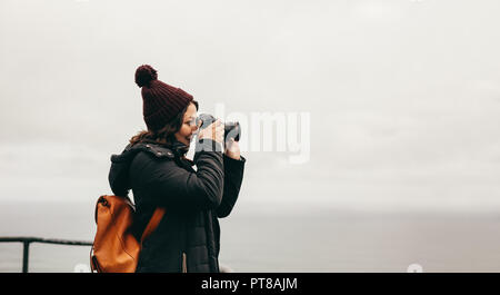 Vue de côté de la femme de prendre des photographies d'un paysage avec son appareil photo reflex numérique. Femme dans des peuplements d'usure sur le dessus de la montagne et prend des photos de la Banque D'Images