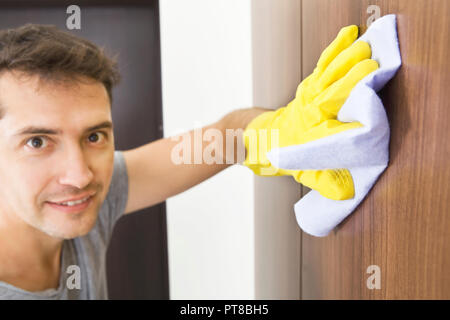 Service de nettoyage. Jeune homme nettoie avec chiffon et gants de protection jaune dans l'appartement Banque D'Images