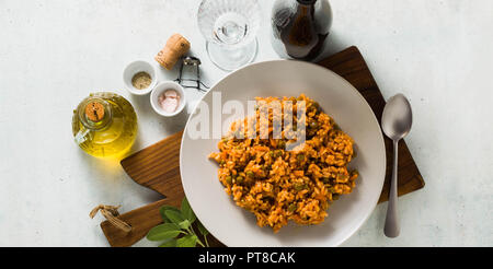 Bannière de risotto italien avec une sauce tomate et pois verts, servi dans une assiette sur une planche à découper en bois et une bouteille de vin mousseux rouge M classique . Banque D'Images