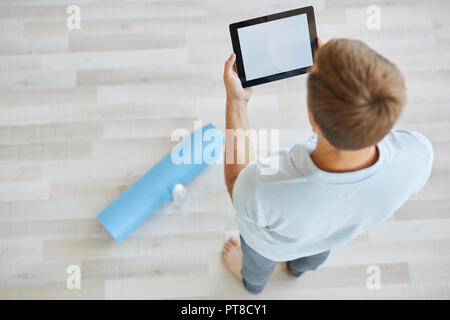 Jeune homme de activewear debout sur le plancher lors de la recherche des videos de séance d'entraînement dans le net Banque D'Images