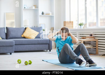 Jeune homme en vêtements d'assise sur le sol avec ses mains derrière la tête et faire des sit-ups Banque D'Images