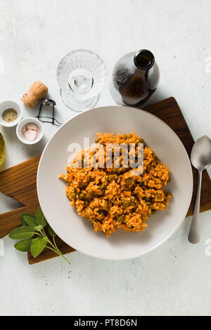 Risotto italien avec une sauce tomate et pois verts, servi dans une assiette sur une planche à découper en bois et une bouteille de vin mousseux rouge . classic Mediterrane Banque D'Images