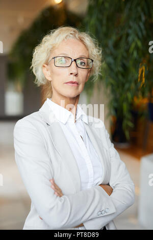 Succès d'affaires graves confiant âgées dame à lunettes looking at camera fièrement et d'une barrière sur la poitrine Banque D'Images