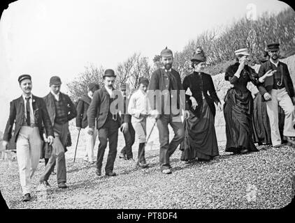 Photographie prise à la fin de l'époque victorienne agroup montrant des gens se promener le long d'une plage de galets quelque part en Angleterre. Typique de la mode montre la période. Banque D'Images