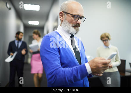 Serious mature businessman in formalwear textos en son smartphone à la rupture dans la salle de conférence Banque D'Images