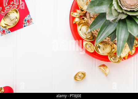 Le nouvel an chinois ang pow concept.Vue de dessus de l'ananas avec groupe de lingots d'or dans le bac rouge sur table en bois blanc.sur moyenne des lingots riches. Banque D'Images