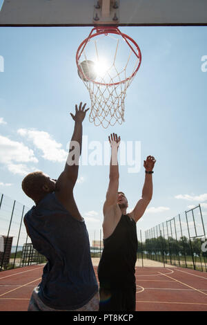 Portrait d'action de deux jeunes hommes jouant au basket-ball et le saut par hoop against blue sky éclairée par la lumière du soleil Banque D'Images