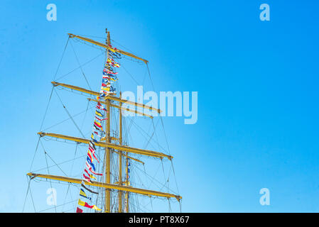 Nautique voile coloré drapeaux au vent des lignes d'un mât voilier dans Ciel bleu rétro-éclairé par le soleil. Banque D'Images