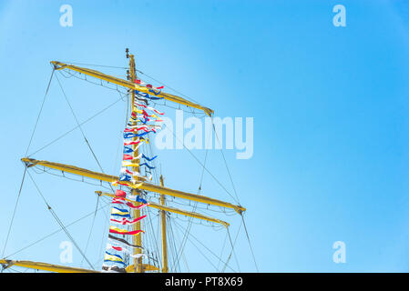 Nautique voile coloré drapeaux au vent des lignes d'un mât voilier dans Ciel bleu rétro-éclairé par le soleil. Banque D'Images