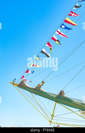 Nautique voile coloré drapeaux au vent des lignes d'un mât voilier dans Ciel bleu rétro-éclairé par le soleil. Banque D'Images