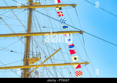 Nautique voile coloré drapeaux au vent des lignes d'un mât voilier dans Ciel bleu rétro-éclairé par le soleil. Banque D'Images