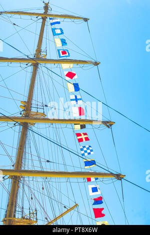 Nautique voile coloré drapeaux au vent des lignes d'un mât voilier dans Ciel bleu rétro-éclairé par le soleil. Banque D'Images