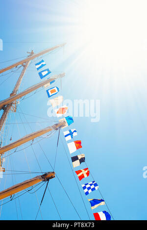 Nautique voile coloré drapeaux au vent des lignes d'un mât voilier dans Ciel bleu rétro-éclairé par le soleil. Banque D'Images