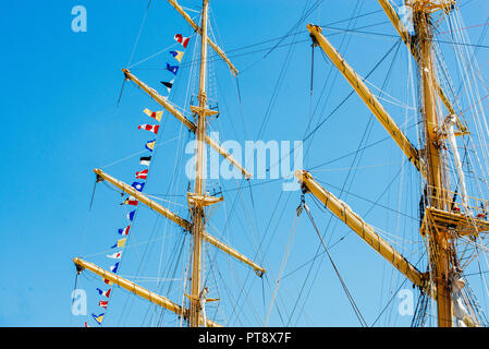 Nautique voile coloré drapeaux au vent des lignes d'un mât voilier dans Ciel bleu rétro-éclairé par le soleil. Banque D'Images