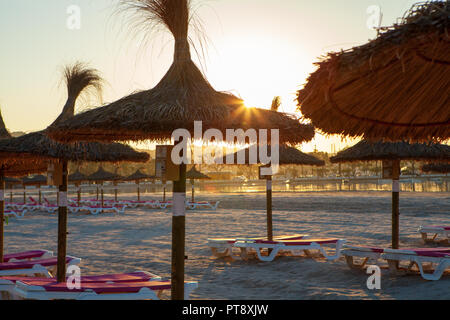 Des chaises vides et des parasols sur la plage d'Alcudia à Majorque au lever du soleil Banque D'Images