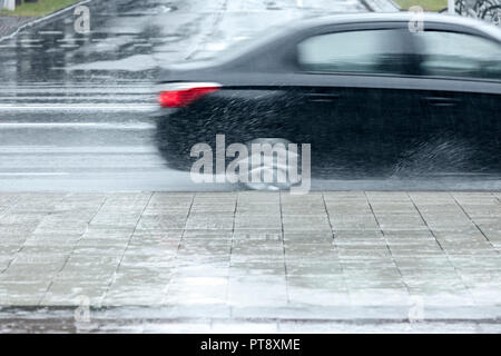 Les éclaboussures d'eau de la voiture roues d'un véhicule à grande vitesse sur route inondée pendant la pluie Banque D'Images