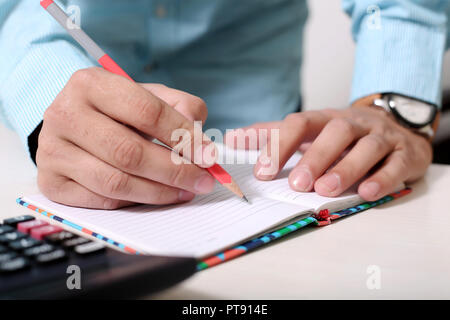 Homme tenant un crayon dans la main avec bloc-notes et calculatrice sur la table. Banque D'Images