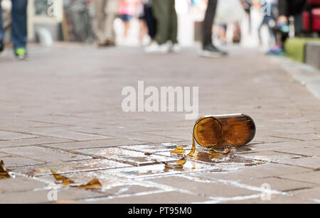 Un flacon de verre brun de bière cassée sur le sol du trottoir rue avec des personnes floues en arrière-plan. Banque D'Images