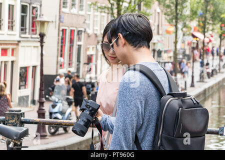 Amsterdam, Pays-Bas, Juillet 21th, 2018 : un couple à la recherche d'Asie les photos sur leur marche de l'appareil photo sur un pont dans le centre-ville d'Amsterdam. Banque D'Images