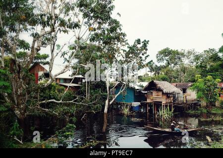 Des maisons sur pilotis sur le fleuve Amazone en Colombie avec un homme sur une pirogue Banque D'Images