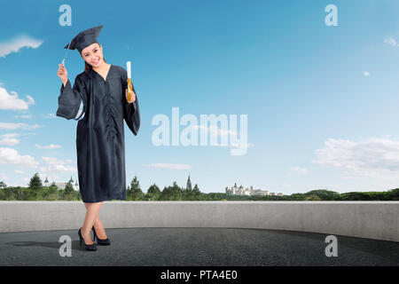 Smiling asian girl in graduation gown et hat standing at outdoor Banque D'Images