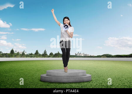 Belle asiatique businesswoman giving speech avec mégaphone sur podium Banque D'Images