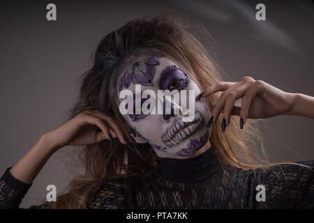 Portrait d'une fille avec un masque peint d'une personne morte sur son visage, isolé sur un fond sombre. Halloween de Banque D'Images