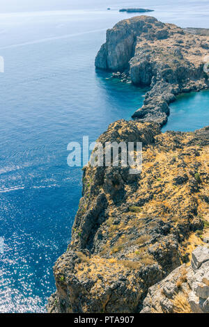 Photo verticale avec vue vers le bas sur les récifs rocheux couverts par de l'herbe sèche et avec la mer bleu autour. Reef est à l'acropole, dans la ville de Lindos s Banque D'Images