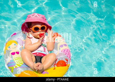 Adorable Baby Girl Wearing Hat et lunettes de sucer un binky sur l'eau bleue Banque D'Images