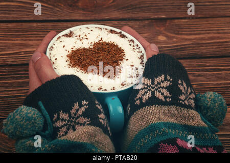 Close up femme deux mains tiennent et Big hug pleine tasse de Cappuccino, Latte avec coeur en chocolat sur mousse de lait sur la table en bois brun, haut Banque D'Images