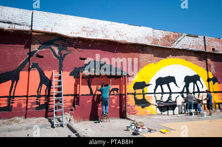 Avec la Bay Area muralistes Projet Mural peindre une scène de savane à l'arrière de l'ancienne usine de Sausage Co. Côte West Oakland le 26 juillet 2017. Banque D'Images